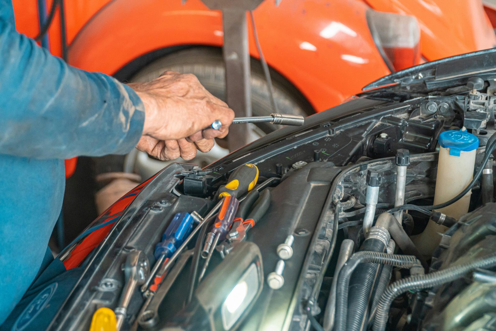 Mechanic performing maintenance on a car engine in a garage setting, using various tools.