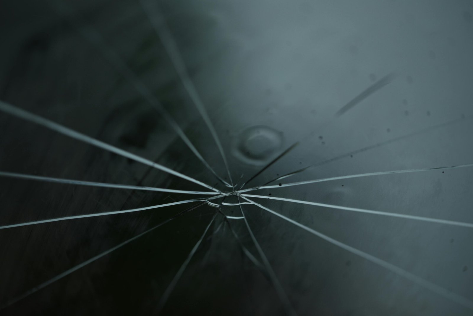 A detailed shot of cracked glass with radiating lines on a moody background.